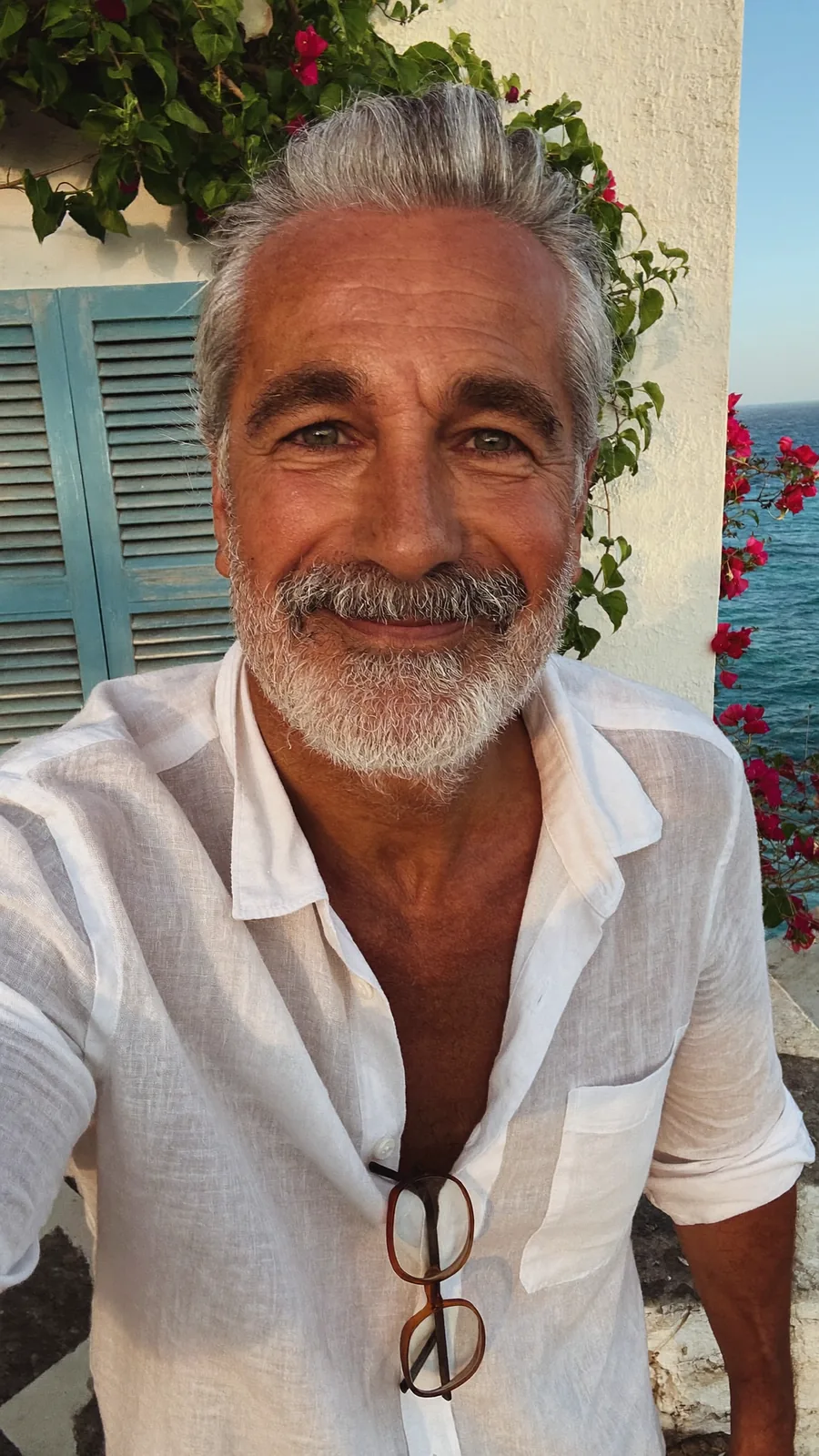 The hotel host, a silver-haired man in a white linen shirt, smiling on the terrace