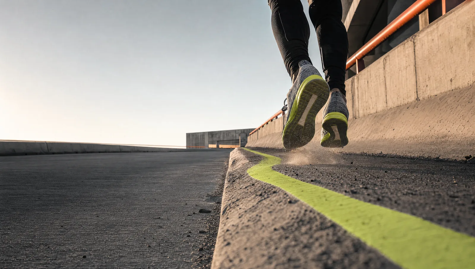 Low angle of a runner's shoes on a concrete overpass, a painted lime line along the curb