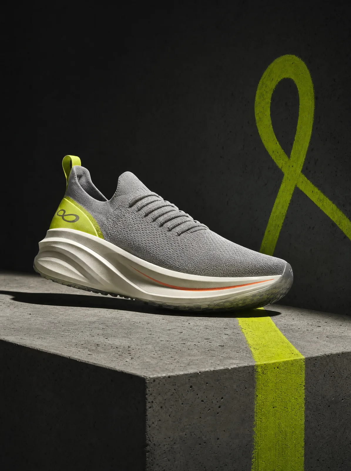 The Lopeline daily trainer: fog-grey knit upper, lime heel, off-white rocker midsole with orange stripe, on a concrete plinth crossed by a lime line