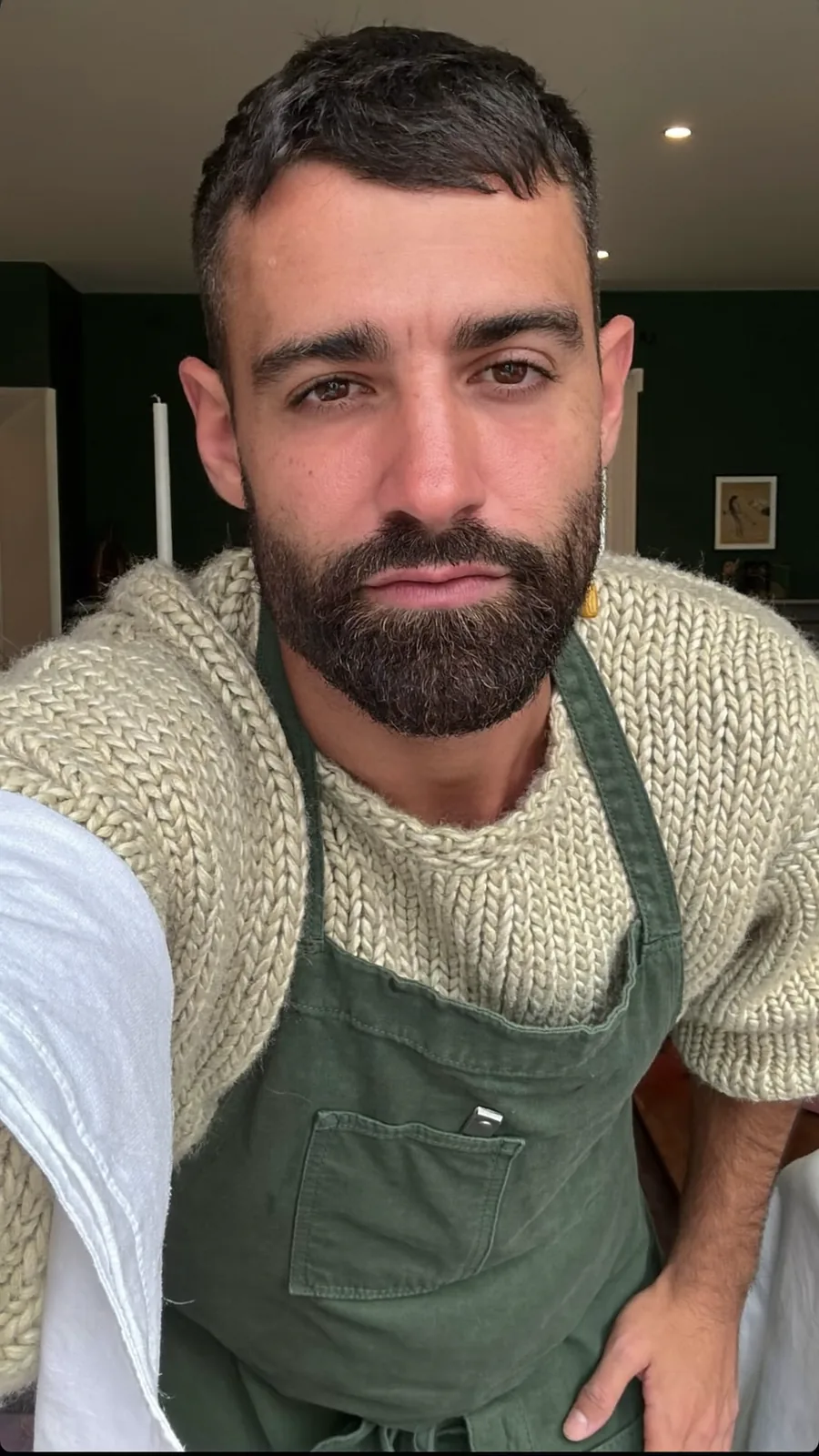 The maître d': a bearded man in an oatmeal sweater and forest-green apron, deadpan to camera
