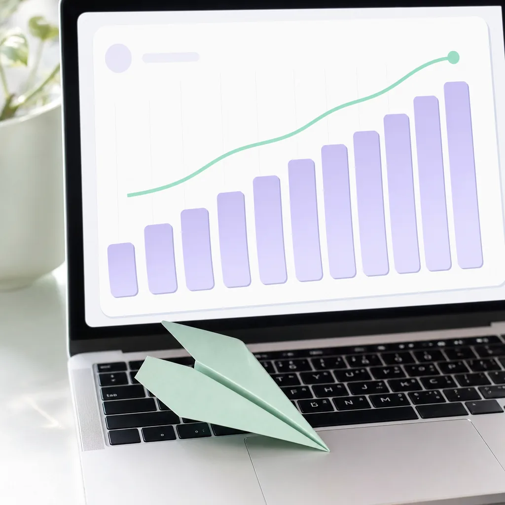 A laptop showing an abstract rising line and bar chart, a mint paper plane landed on the keyboard